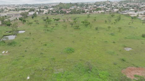 AERIAL---Green-field-and-cityscape-in-Jos-Plateau,-Nigeria,-forward-shot