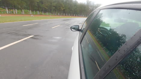 Suction-Cup-Shot-Of-A-White-Car-Driving-On-A-Wet-Private-Course