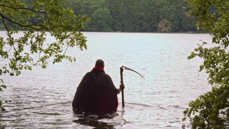 Man-with-black-cloak-and-scythe-plunging-into-the-water-of-a-lake