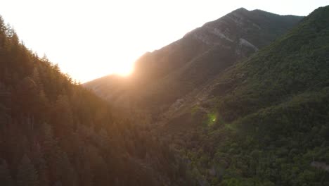 Sunset-Sun-Rays-Peaking-over-Mountain-Ridge-in-Millcreek-Canyon,-Utah---Aerial
