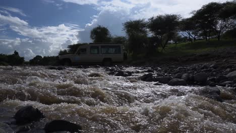 Niedrige-Sichtaufnahme-Eines-Safarifahrzeugs,-Das-Eine-Kleine-Wasserschnelle-In-Natron-Tansania-Mit-Wunderbarem-Himmel-überquert