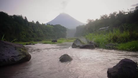 Mountain-water-stream-flowing-between-rocks-with-volcano-that-emits-smoke---beautiful-nature-footage-in-jungle