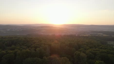Sonnenuntergangsdrohnenflug-über-Wälder-Und-Berge-Mit-Einem-Dorf-Im-Tal