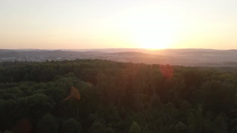 Aufsteigende-Drohnenaufnahmen-über-Einem-Riesigen-Wald-Bei-Einem-Orangefarbenen-Sonnenuntergang-Mit-Bergen-Im-Hintergrund