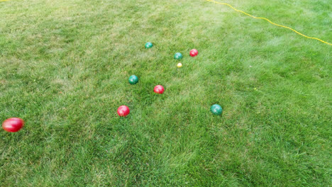 Overview-shot-of-red-heavy-metal-ball-thrown-on-ground-while-playing-traditional-boules-game-on-target