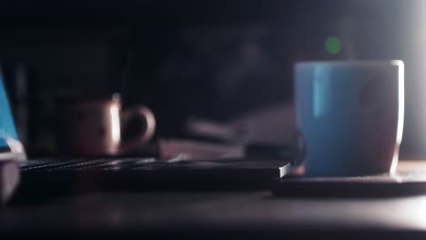 Eine-Dampfende-Tasse-Nachttee-Oder--kaffee-Neben-Einem-Offenen-Computer-Und-Lampenlicht