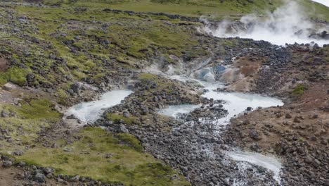 Aerial-approaching-shot-of-Olkelduhals-geothermal-area-with-sulfur-lakes-and-mud-pots-in-Iceland---Fumes-ascending-into-sky