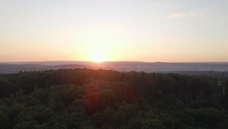 Schnell-Fliegende-Aufnahmen-über-Einem-Riesigen-Wald-Bei-Einem-Orangefarbenen-Sonnenuntergang-Und-Wunderschönen-Sonneneruptionen-In-Den-Bildern-Mit-Bergen-Im-Hintergrund