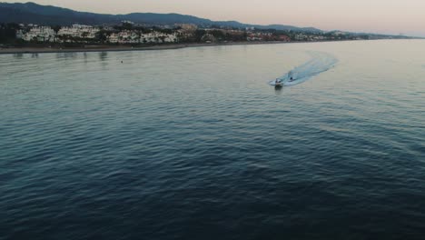 Fast-boat-passing-by-near-the-coastline-of-Marbella,-Spain,-during-sunset