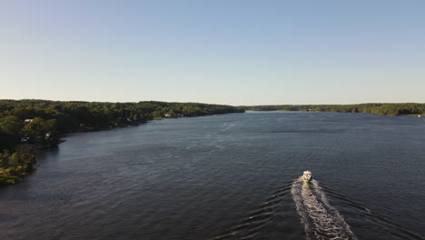 Aerial-shot-of-looking-down-at-speed-boat-on-the-Kennebec-River-Maine,-overtaking-boat,-exits-bottom-right-of-frame
