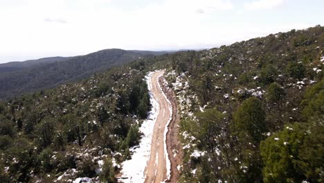 Fast-push-in-aerial-shot-of-dirt-road-in-the-middle-of-the-snowy-woods-in-Oncol-Park,-Chile