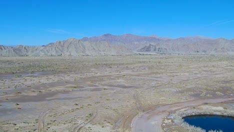 View-of-a-drone-descending-over-plain-land-showing-a-mountain-in-the-background-and-a-river-at-the-side