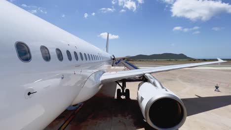 Tilt-down-view-from-front-door-of-fuselage-wing-and-engine-of-airplane-parked-at-Ibiza-Balearic-island-airport-with-stairs-attached-on-sunny-day