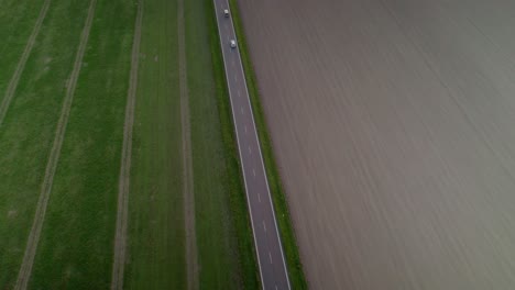 Aerial-drone-shot-following-cars-driving-through-road-among-agriculture-fields-and-green-countryside-at-daytime