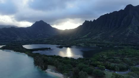 Aerial-push-in-shot-of-Kaneohe-Bay-and-Molii-Fishpond-as-the-sun-sets-behind-a-dramatic-mountain-backdrop-in-tropical-paradise