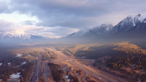 Canmore-Alberta-mountain-range-Canadian-rockies-surrounding-highway-and-overpass-aerial-sunrise-drone-shot-pan-away