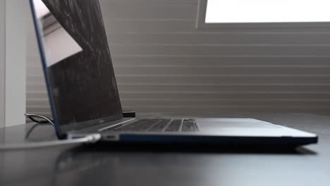 Seitenansicht-Eines-Laptops-Auf-Einem-Schreibtisch-Mit-Tastatur-Und-Einem-Weißen-Kabel,-Das-Zum-Aufladen-Eingesteckt-Ist