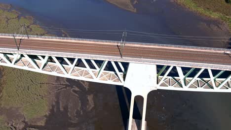 Fliegen-über-Die-Eisenbahnbrücke-Mit-Stromleitungen-über-Den-Fluss-Ulla-Bei-Niedrigem-Wasserstand,-Tief-Fliegende-Möwen,-Zenitale-Drohne-Schießen-Vorwärts,-Catoira,-Galizien,-Spanien