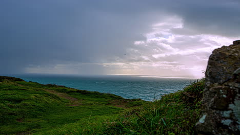 Zeitraffer-Dunkler-Wolken,-Die-Im-Grünen-Küstengebiet-über-Den-Ozean-Fliegen