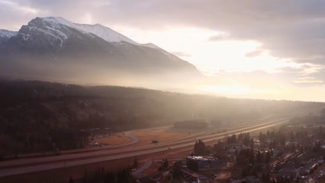 Dramatic-fast-drone-aerial-crane-down-as-golden-light-beams-over-valley-surrounded-by-mountain-range