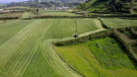 Tractor-harvesting-green-field-in-countryside-of-Azores,-aerial-view