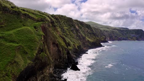 Rugged-grassy-coastline-cliffs-over-Atlantic-ocean-in-Azores,-flyover