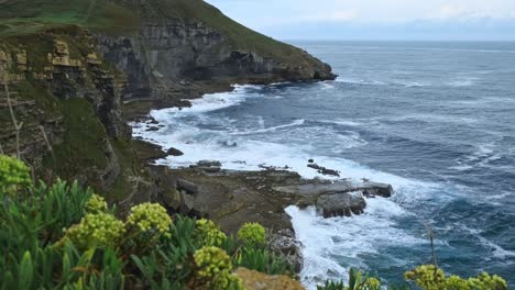 On-the-island-of-Isla-in-Cantabria,-the-blue-Cantabrian-sea-can-be-seen-from-the-rocky-cliff's-edge
