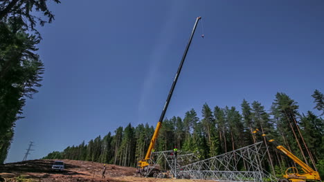 Time-lapse-of-a-crane-erecting-a-high-voltage-tower-in-a-forest-clearcut-with-several-people-managing-it