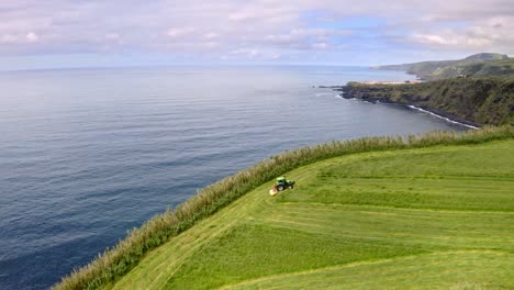 Tractor-cutting-grass-in-field-on-steep-sea-cliff,-Azores,-aerial-view