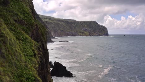 Waves-crashing-on-high-rugged-coastal-cliffs-in-Azores,-flyover-shot