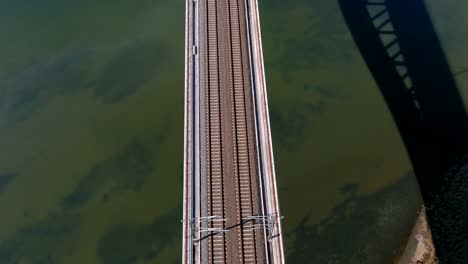 Flying-over-the-center-of-the-railway-bridge-over-the-marsh-and-the-turquoise-blue-water-of-the-Ulla-River-on-a-sunny-day,-rolling-overhead-drone-shot-up-traveling-forward,-Catoira,-Galicia,-Spain