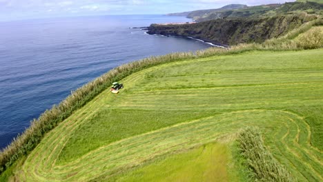 Tractor-cutting-field-grass-on-sea-coast-cliffs-of-Azores,-flyover