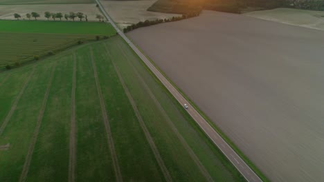 Aerial-drone-shot-of-a-car-driving-on-a-highway-with-a-view-of-the-fields-on-either-side