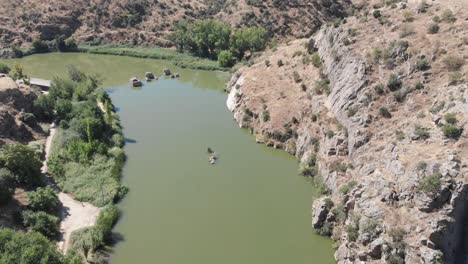 Drone-overflying-a-green-looking-Tajo-River-in-Toledo,-Spain