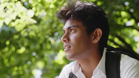 Handsome-Indian-guy-sitting-under-tree-foliage-on-sunny-day-wearing-white-shirt