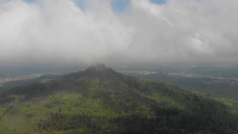 Descending-aerial-drone-view-from-Zellerhorn-looking-towards-the-Hohenzollern-Castle-under-the-fog-in-the-Black-Forest,-Germany