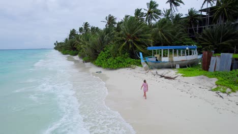 Aerial-view-of-girl-walking-in-tropical-beach-as-turquoise-sea-waves-breaks-in-shore