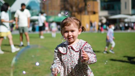 Smiling-little-baby-girl-smashing-bubbles-with-hands-in-a-playground-on-summer-day