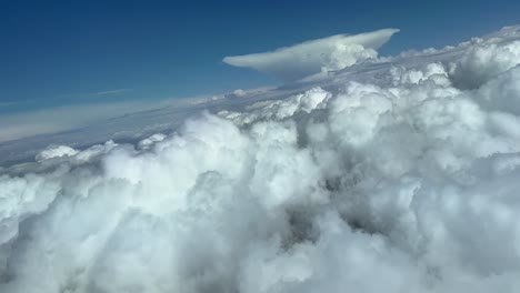Impressive-view-from-a-jet-cockpit-during-a-right-turn-to-avoid-bad-weather-ahead,-in-a-sky-plenty-of-cumulus-and-a-huge-cumuloninbus-anvil-shape-at-the-back