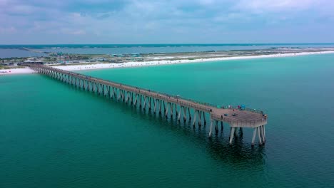 Aerial-drone-panning-right-view-of-the-Navarre-Beach-Florida-Pier-with-some-dark-clouds-and-the-white-sand-beach-in-the-background