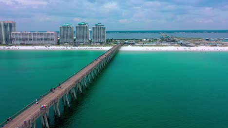Aerial-view-flying-down-the-Navarre-Beach-FL-Pier-looking-at-the-beautiful-white-sand,-board-walk,-and-the-water-tower