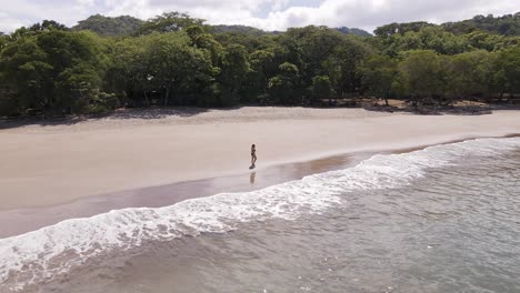 Young-white-woman-in-bikini-walking-along-the-lush,-empty-shore-of-Playa-Real-in-Guanacaste,-Costa-Rica