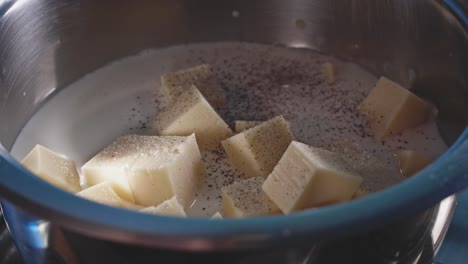 Cubed-Cheese-And-Milk-Boiling-In-A-Pot,-Sprinkled-With-Salt-And-Pepper