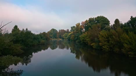 Eine-Drohne-Fliegt-über-Die-Oberfläche-Einer-Flussmündung-Mit-Ufern,-Die-Wunderschön-Mit-Den-Blättern-Von-Herbstbäumen-Gefärbt-Sind