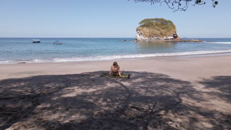 Mujer-Joven-En-Bikini-Sentada-Debajo-De-Un-árbol-En-Una-Playa-Vacía-En-Costa-Rica