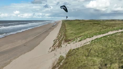 Static-Aerial-Drone-Shot-of-Paraglider-Riding-A-Strong-Wind-on-a-Sunny-Beach