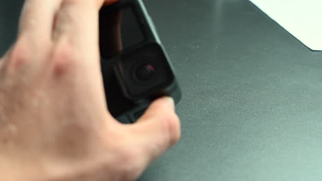 A-filmmaker-holds-an-action-cam-between-his-fingers-with-a-lens,-waterproof-electronical-device