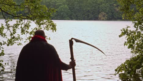 Grim-reaper-with-black-cloak-and-scythe-walks-into-the-water-of-a-lake