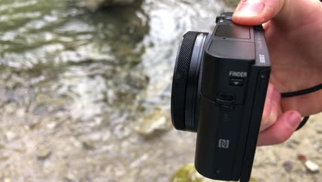 Side-view-of-a-compact-camera-next-to-a-river,-outdoor-filmmaking,-technology