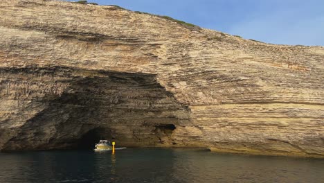 Tourist-boat-comes-out-of-Bonifacio-cliffs-St-Antoine-wide-cave-in-Corsica,-France